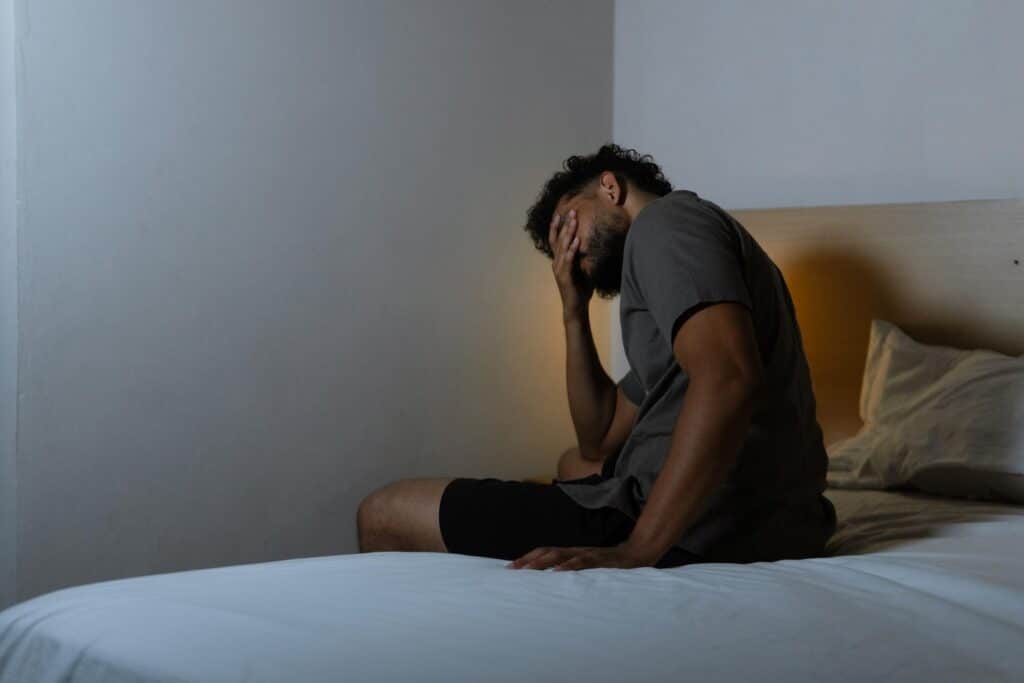 Can Alcohol Withdrawal Kill You? Warning Signs You Should Never Ignore 3 Man sitting on bed, looking distressed. |. alcohol problem